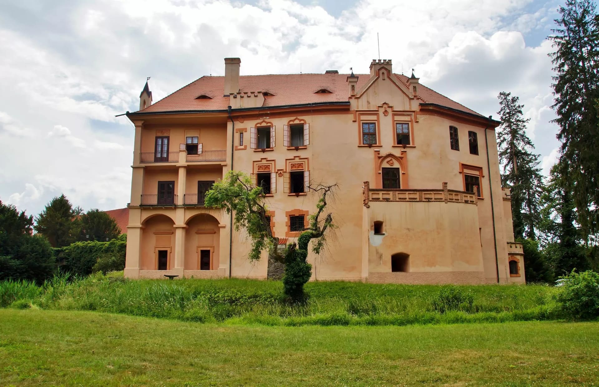 Růžová fasáda zámku Vrchotovy Janovice s lodžiemi a zdobenými štíty od zámeckého parku