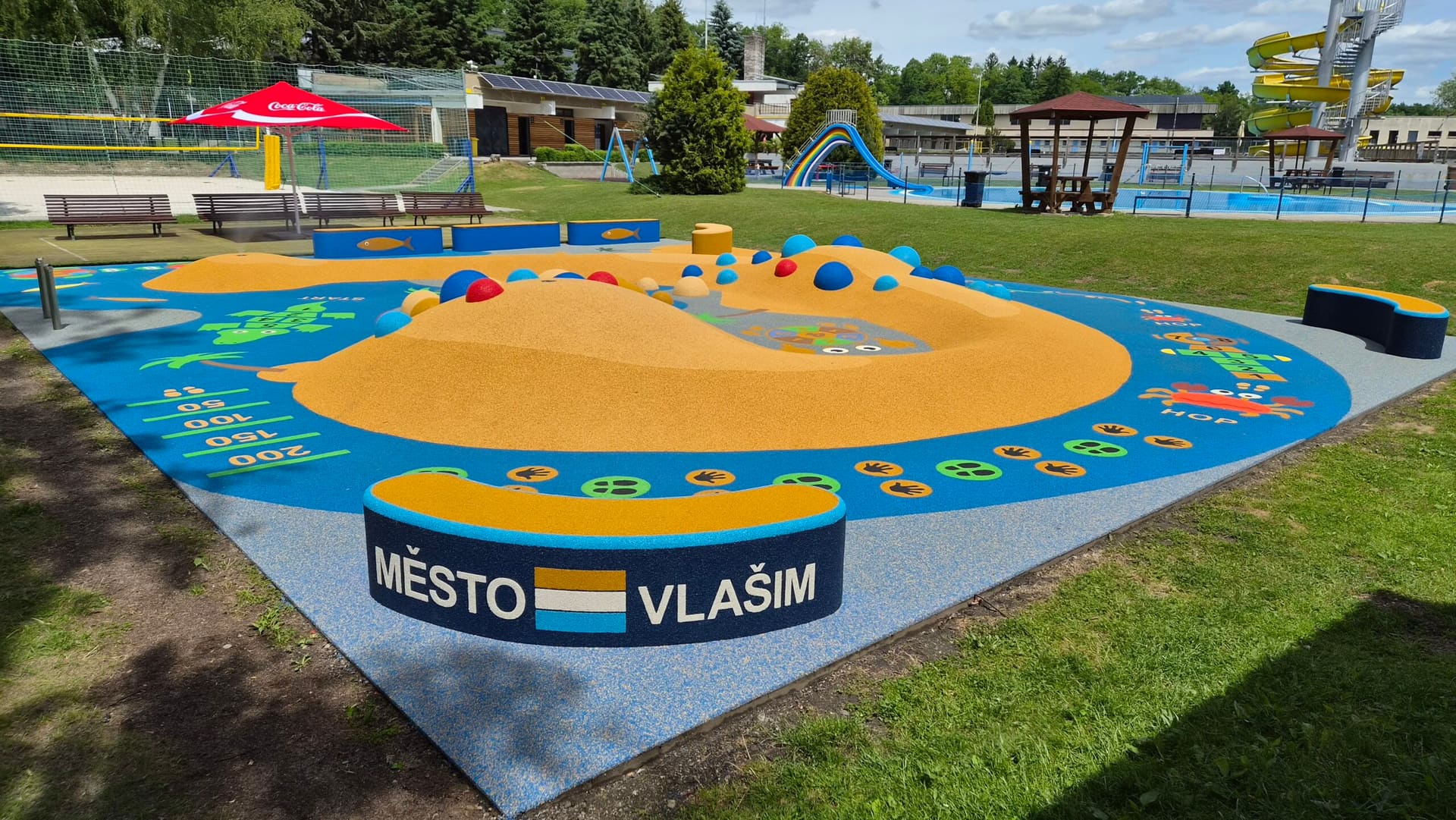 Dětské hřiště s barevným povrchem a nápisem Město Vlašim na koupališti Na Lukách