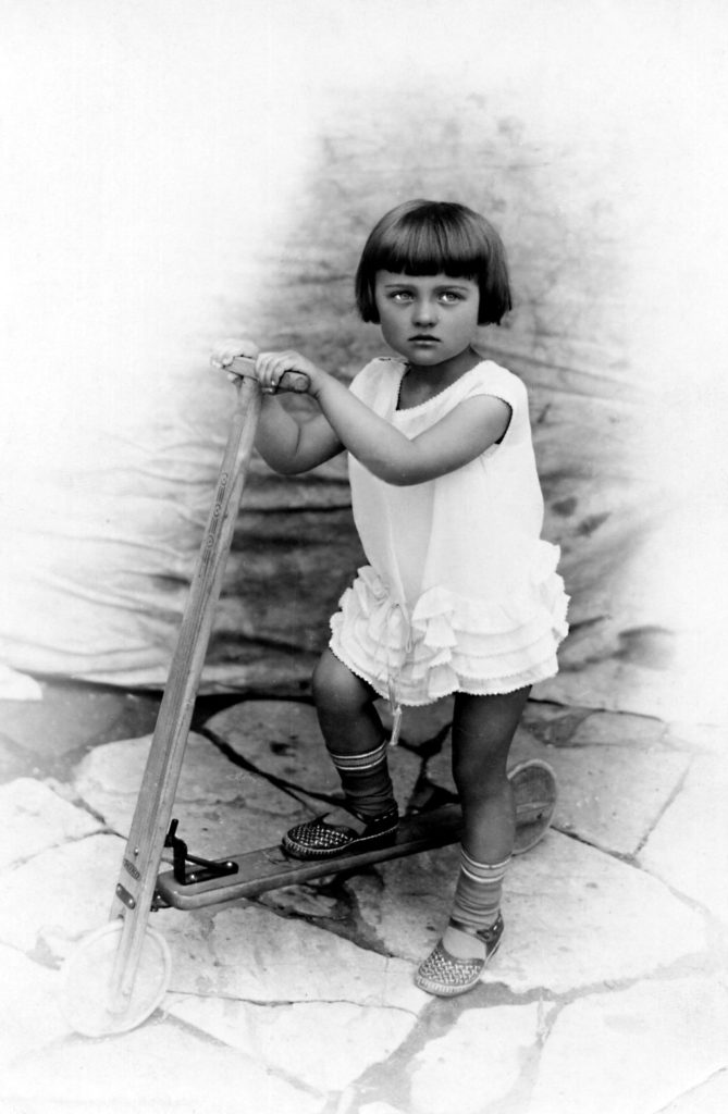 Malá Jarmila Kameníková s koloběžkou před rodinným obchodem ve Vlašimi (1931)