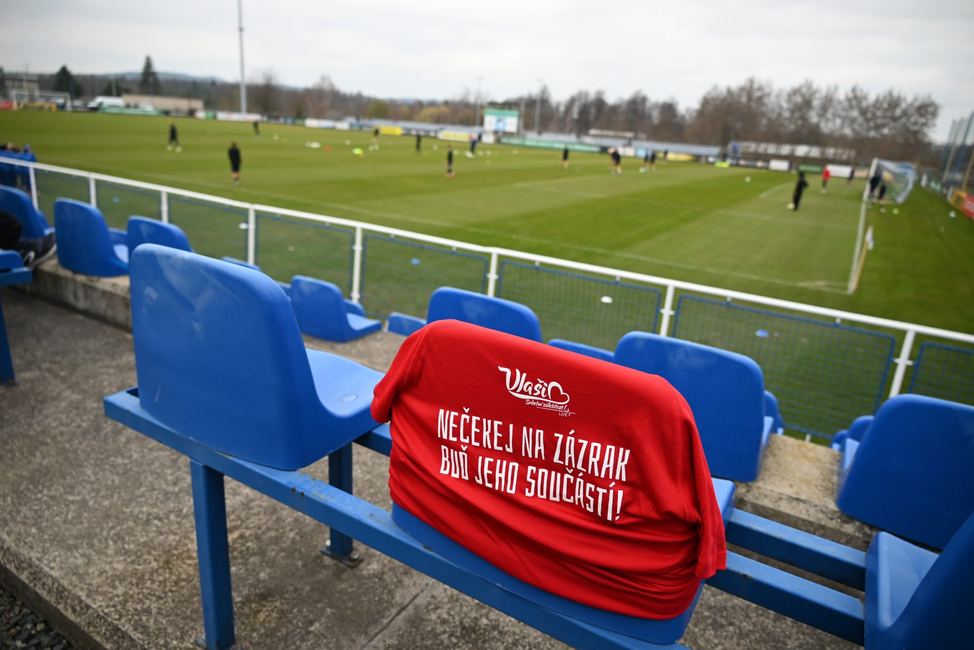 Tribuna stadionu FC Sellier a Bellot Vlašim s fanouškovským tričkem s nápisem Buď jeho součástí